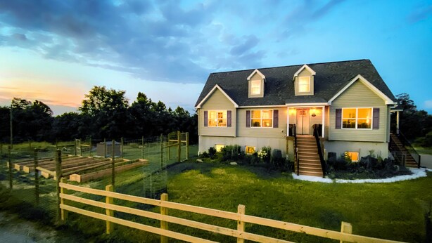 A two-story house with a front porch, a fenced yard, and a staircase leading to the entrance.