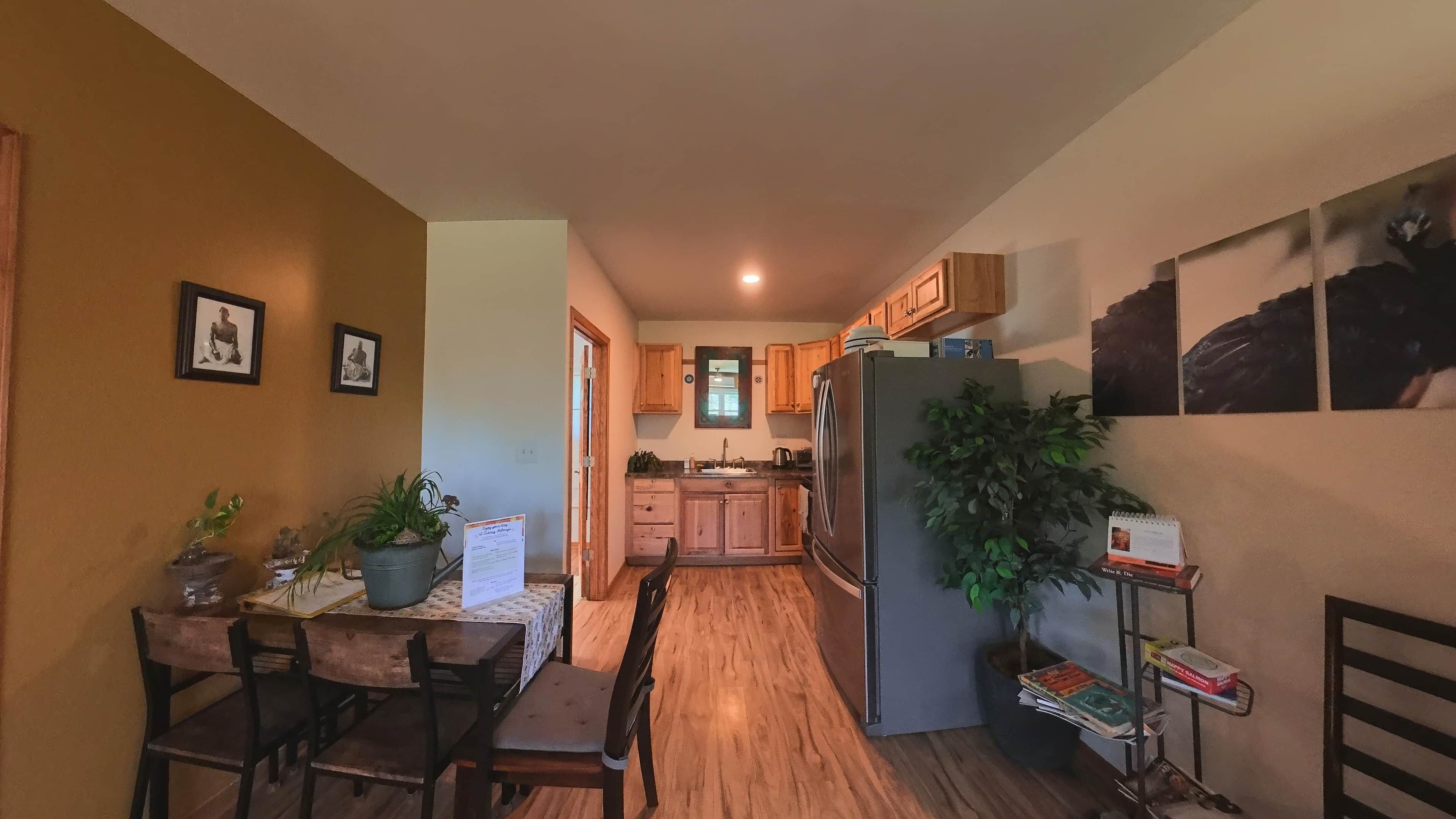 A compact kitchen with wooden cabinets, a refrigerator, and a dining area with a table and chairs.