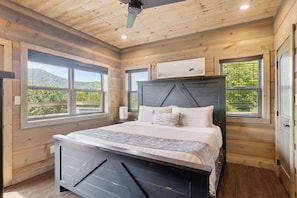 A bedroom with a bed, two windows, a ceiling fan, and a mounted air conditioner.