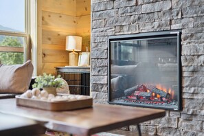 Une cheminée avec une façade en pierre, une table en bois agrémentée d’objets décoratifs et une fenêtre donnant sur un paysage verdoyant.