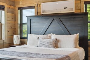 Un dormitorio con una cama grande, un cabecero de diseño geométrico, un cuadro enmarcado sobre la cama y una ventana con persianas.