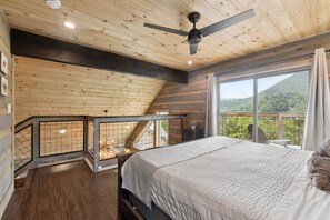 A bedroom with a bed, a ceiling fan, a window with a view of greenery, and a balcony with a railing. - Dreamy Mountain Views + Hot Tub + Movie Room + Dog-friendly + Pool Access (Sevierville)