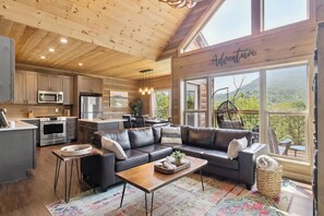 Una cocina moderna con electrodomésticos de acero inoxidable, un comedor con sofá de cuero negro, y ventanas amplias que ofrecen vistas al exterior.