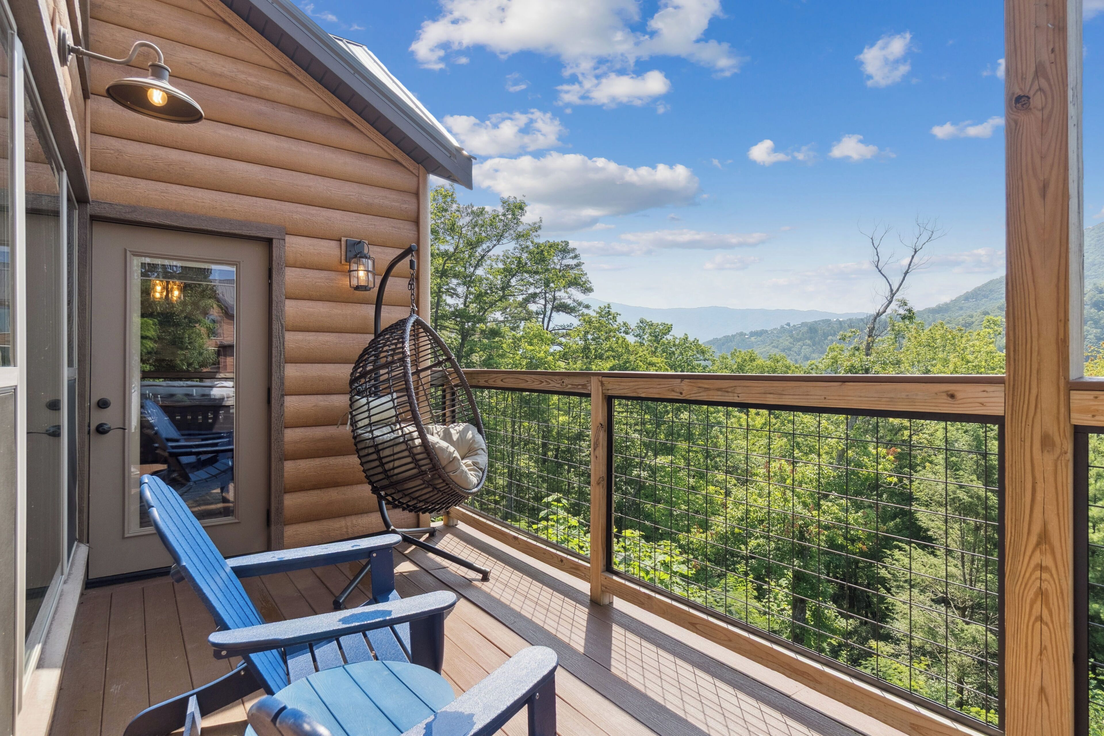 A wooden deck with two blue chairs and a hanging chair, overlooking a forested landscape.