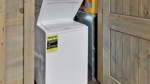 Pequeña lavandería compacta y blanca, con revestimiento de madera, un refrigerador pequeño y una botella de detergente.