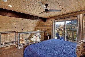 Un dormitorio con una cama grande, un ventilador de techo y vistas a una montaña boscosa a través de una ventana.