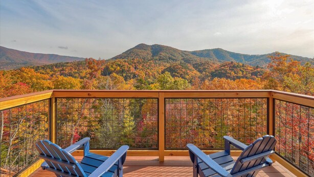 Terraza con dos sillas Adirondack con vistas a una cadena montañosa boscosa.