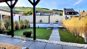 A patio with a table and chairs, a wine glass, and a view of a vineyard in the background. - MoselVilla No 7 (Pommern)