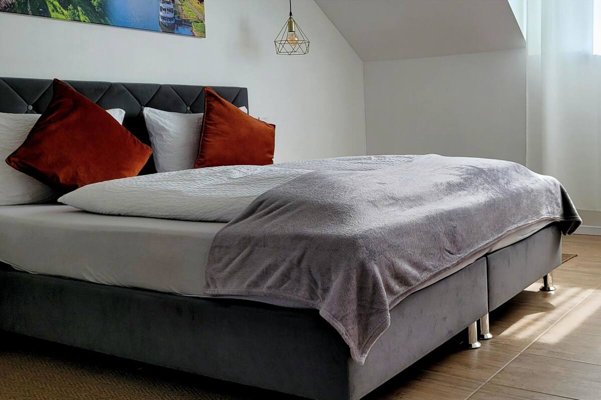 A modern bedroom with a bed, pillows, a chair, and a painting on the wall.