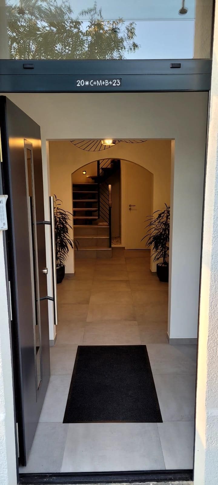 A modern entrance with a black mat, a staircase, and potted plants.