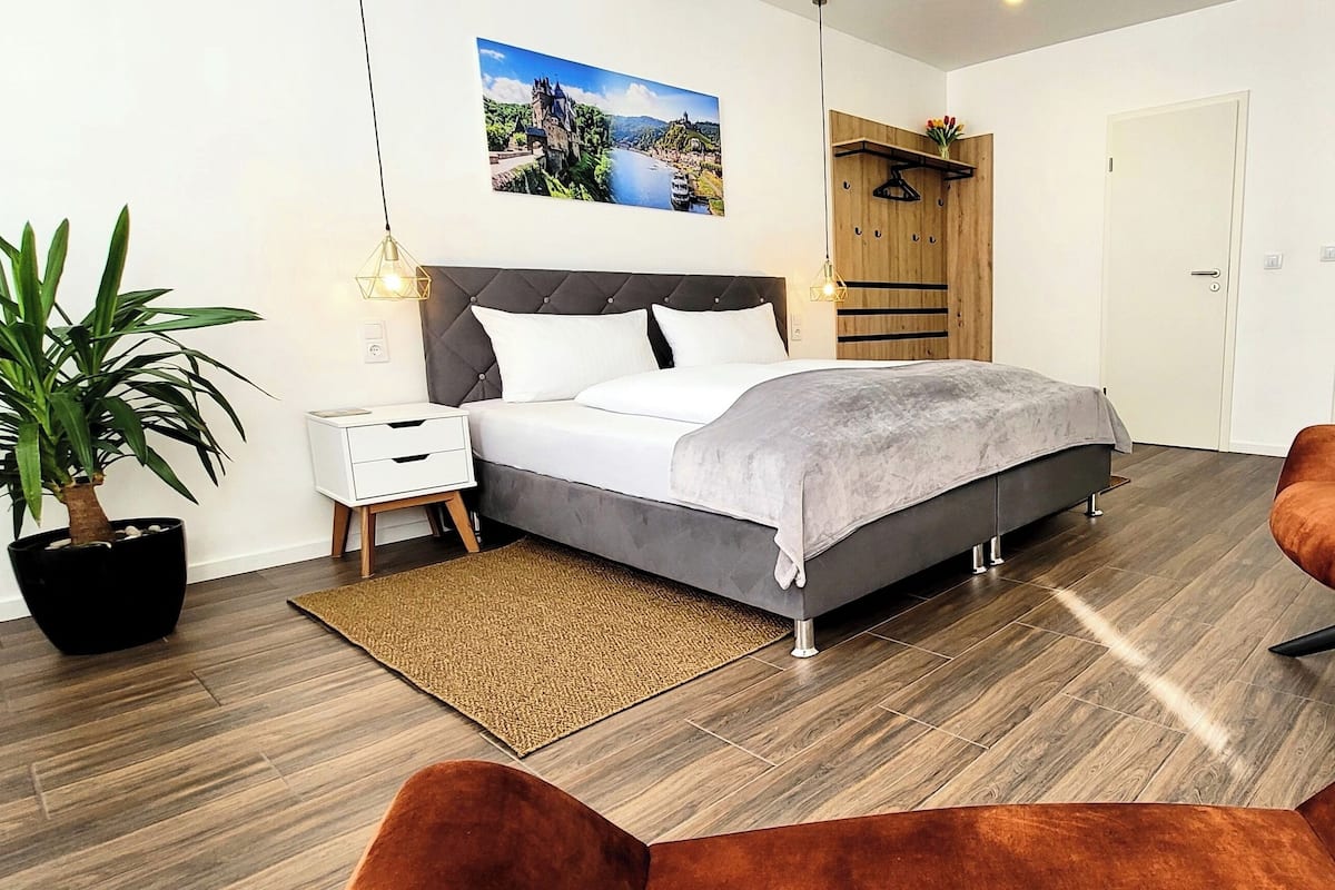 A modern bedroom with a bed, bedside tables, a potted plant, a wooden desk with a bottle of champagne, and a chair.