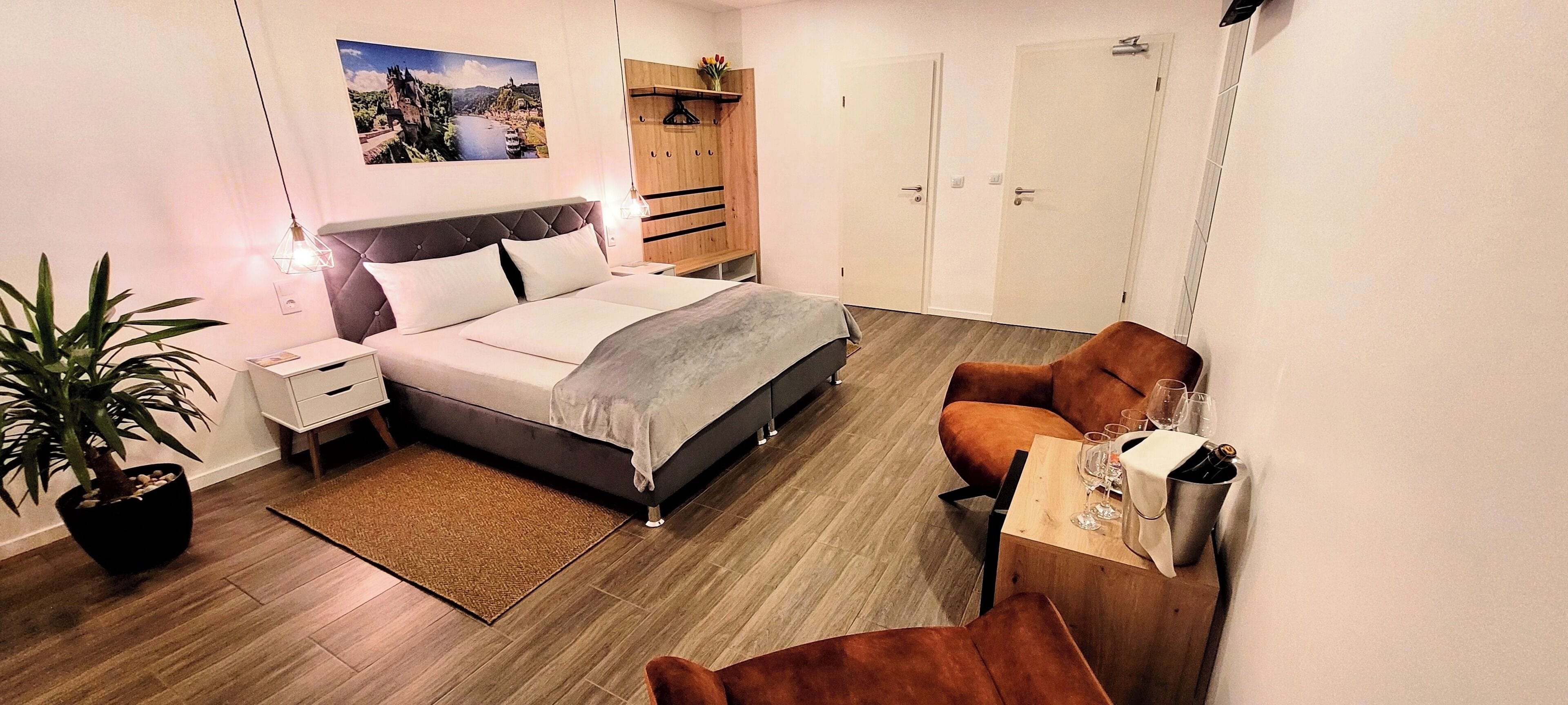 Quarto moderno com cama, mesas de cabeceira, escrivaninha, cadeira, planta em vaso e guarda-roupa.