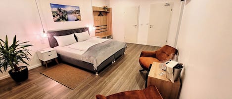 Quarto moderno com cama, mesas de cabeceira, escrivaninha, cadeira, planta em vaso e guarda-roupa.