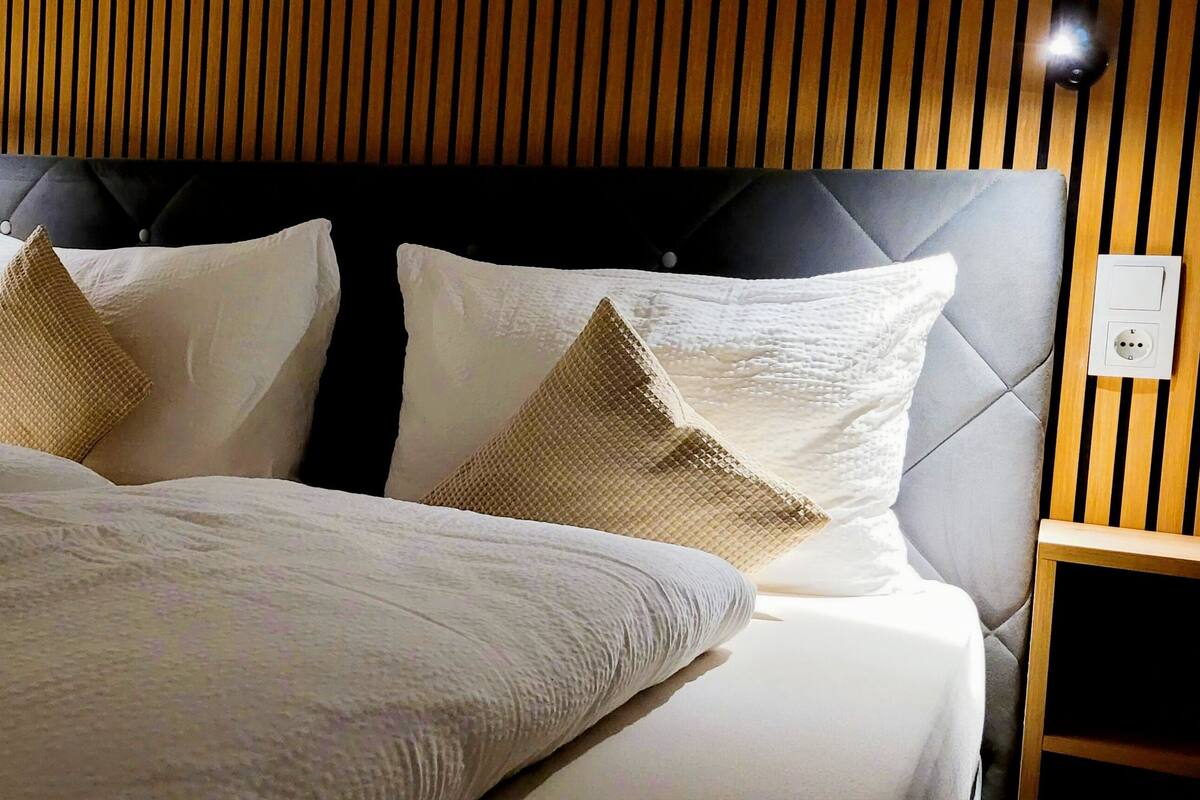 A hotel room with a bed, two nightstands, a wooden headboard, and a wall-mounted light fixture.