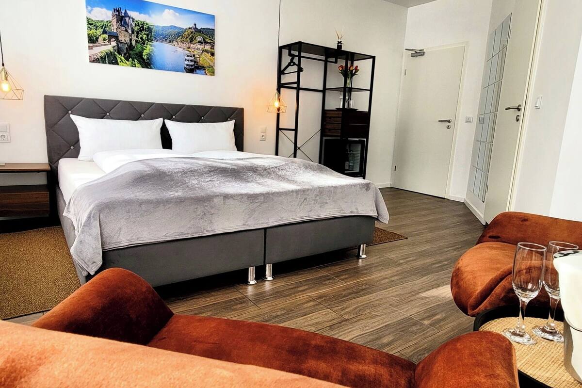 A modern bedroom with a large bed, a nightstand, a bookshelf, and a seating area with a table and chairs.