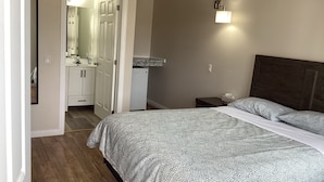Una camera da letto con un letto, un comodino, una lampada a muro e una porta che dà su un bagno.