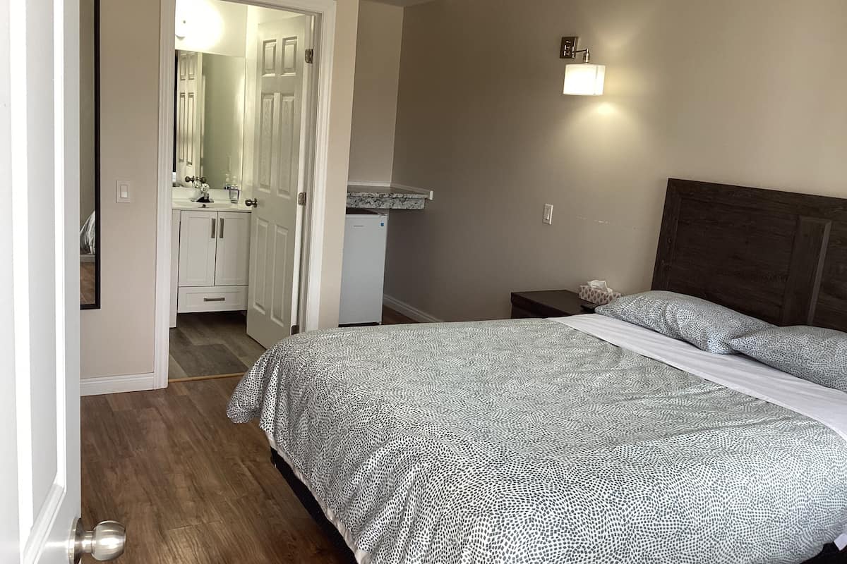 A bedroom with a bed, a nightstand, a wall-mounted light, and a door leading to a bathroom.