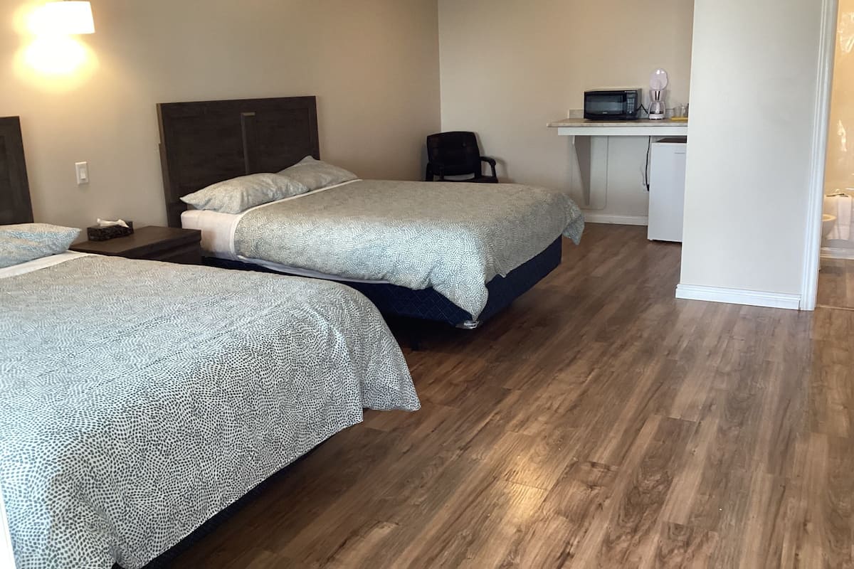 A hotel room with two beds, a desk, a chair, and a microwave.