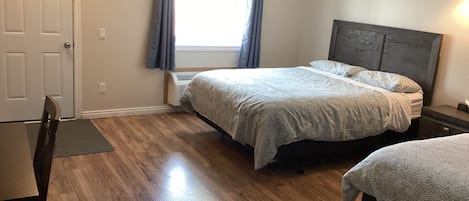 Un dormitorio con cama, mesita de noche, silla y ventana con cortinas.