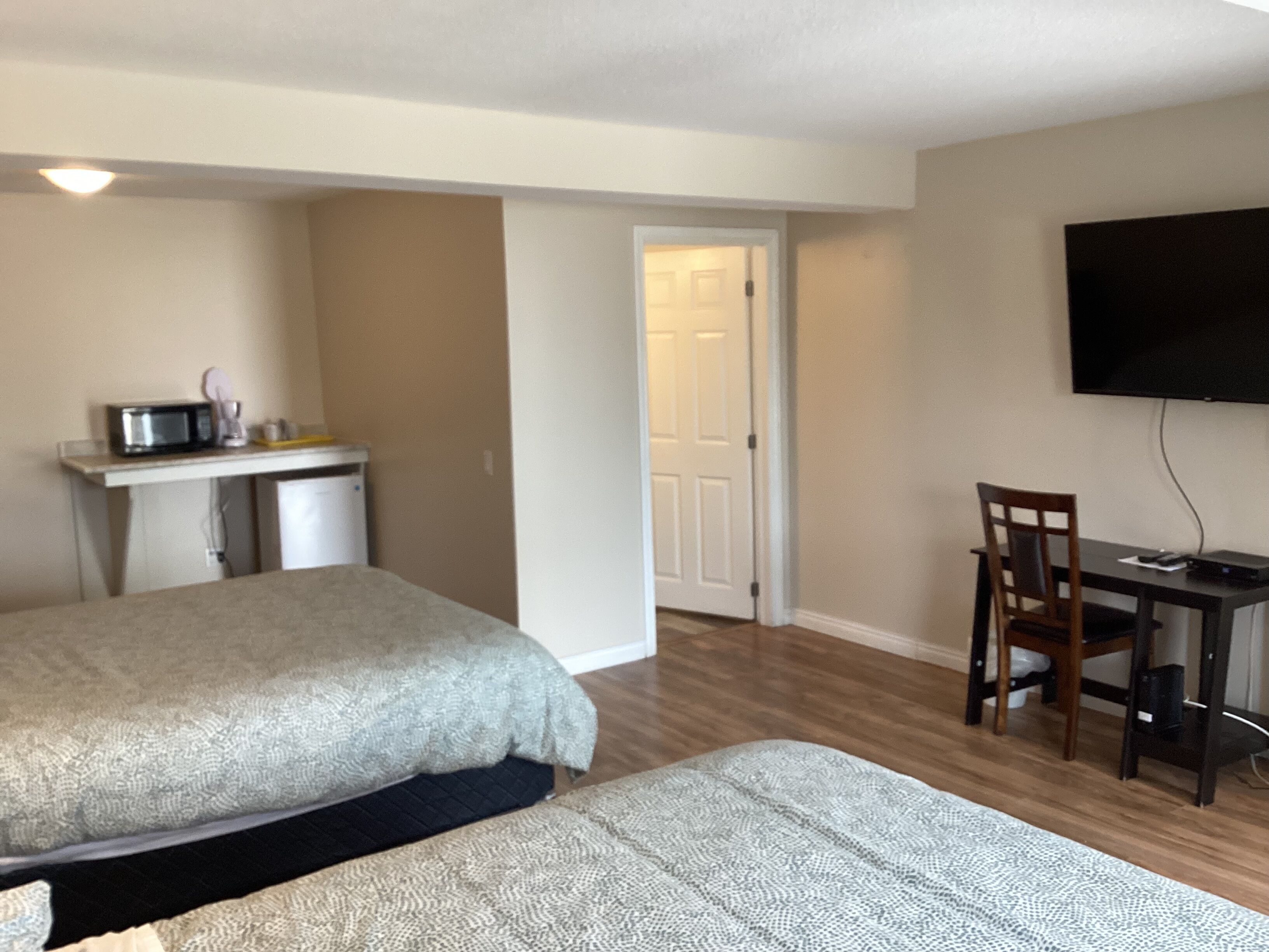 A hotel room with two beds, a kitchenette, a desk with a chair, and a TV mounted on the wall.