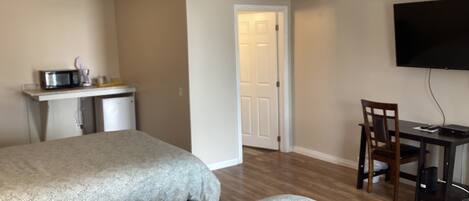 A hotel room with two beds, a kitchenette, a desk with a chair, and a TV mounted on the wall.