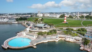 Un hotel frente al mar con piscina, un faro y vistas a la ciudad.