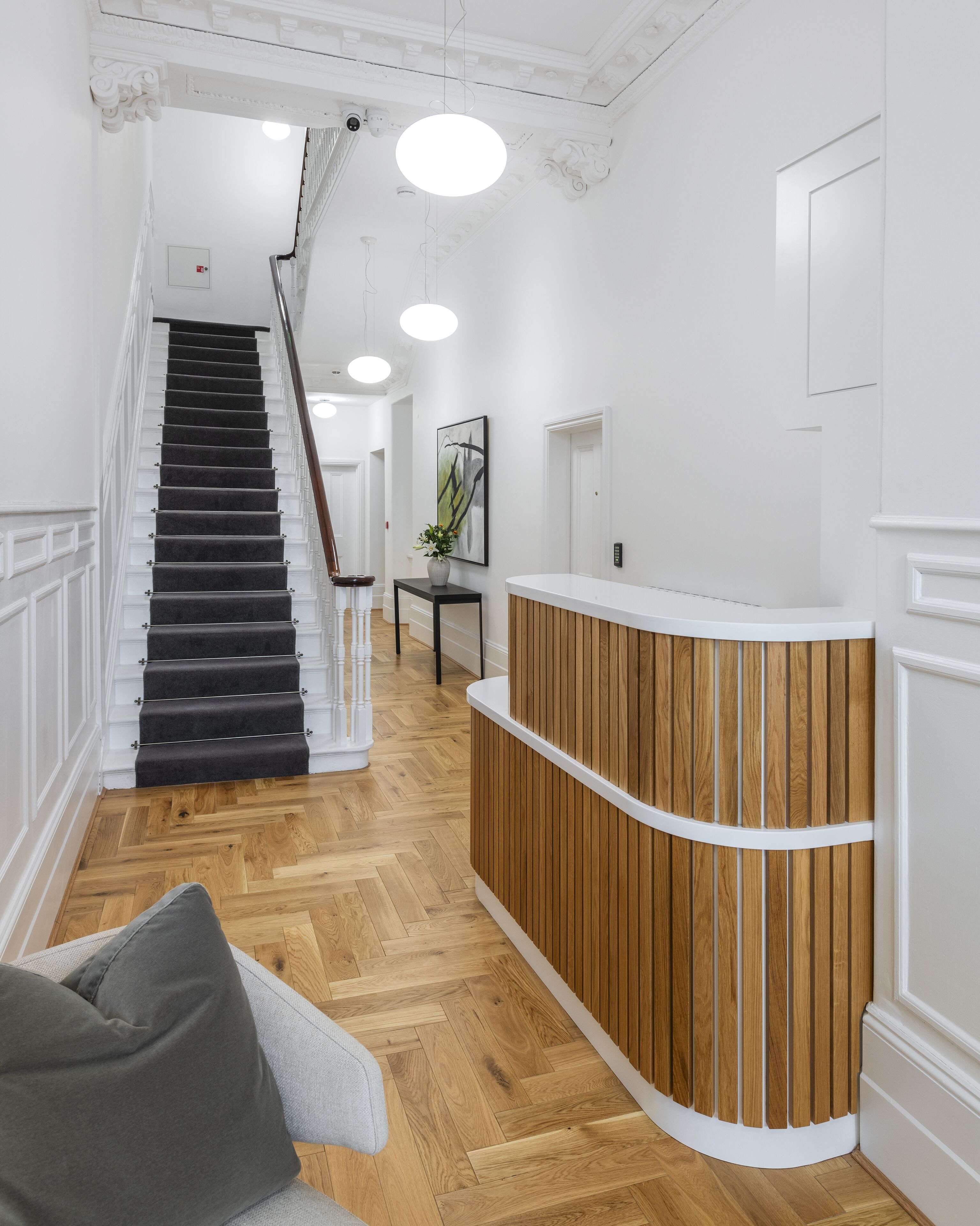 A reception area with a wooden reception desk, a staircase with black carpeted steps, and a herringbone wood floor.