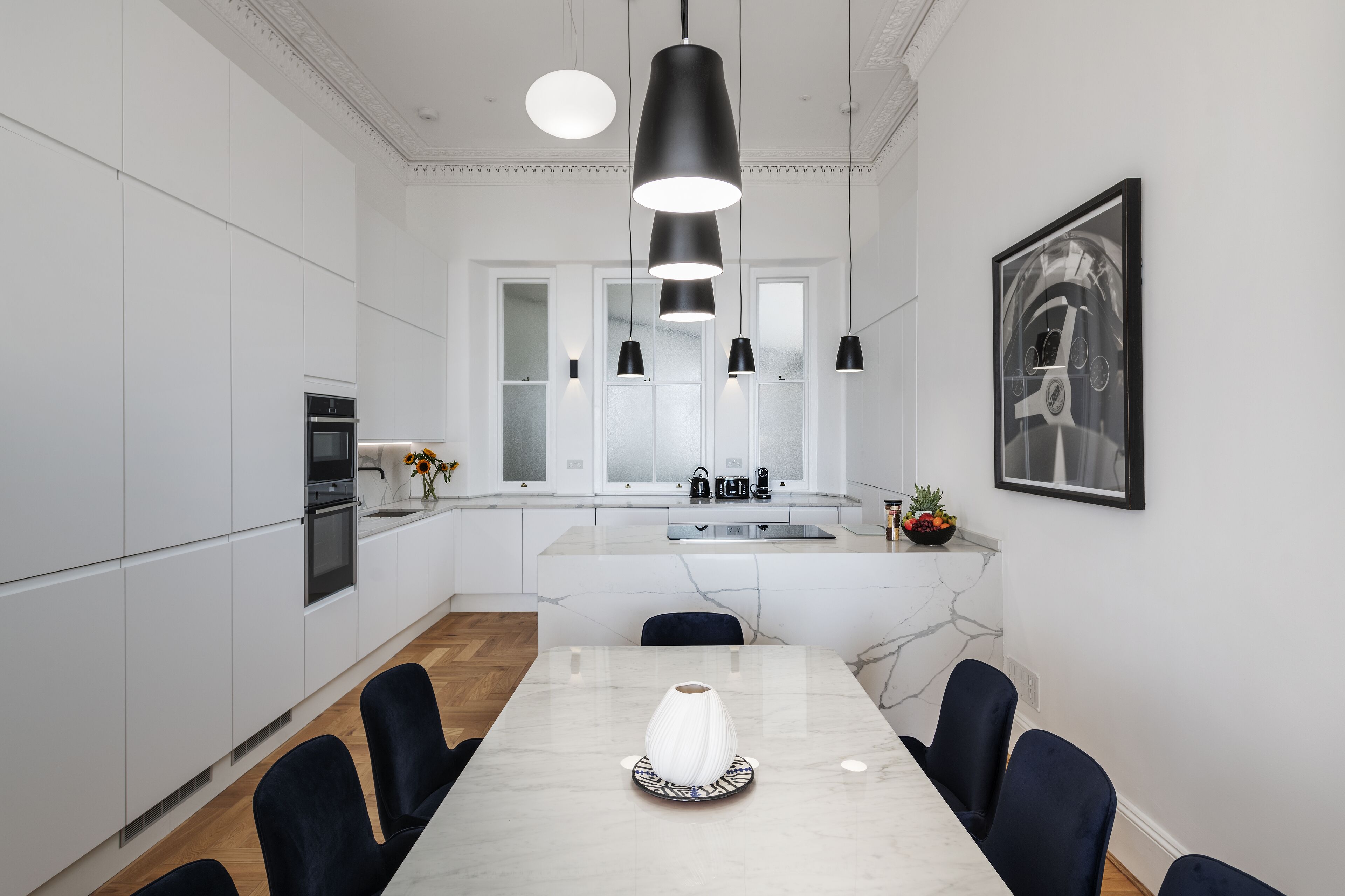 A modern kitchen with white cabinets, a marble countertop, and a dining area with a white table and chairs.