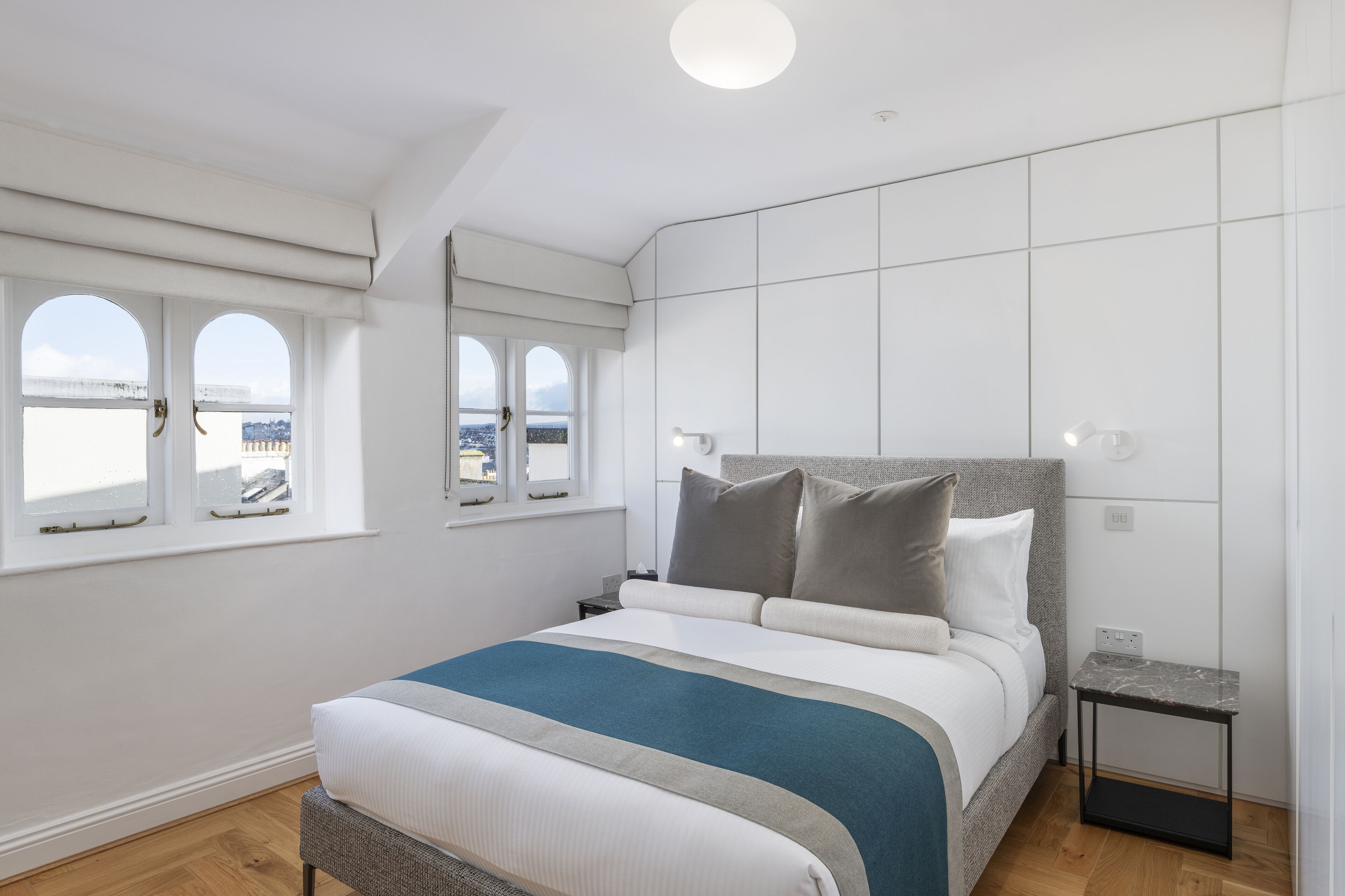 Quarto moderno com uma cama grande, mesa de cabeceira, uma pequena mesa e vista pela janela.