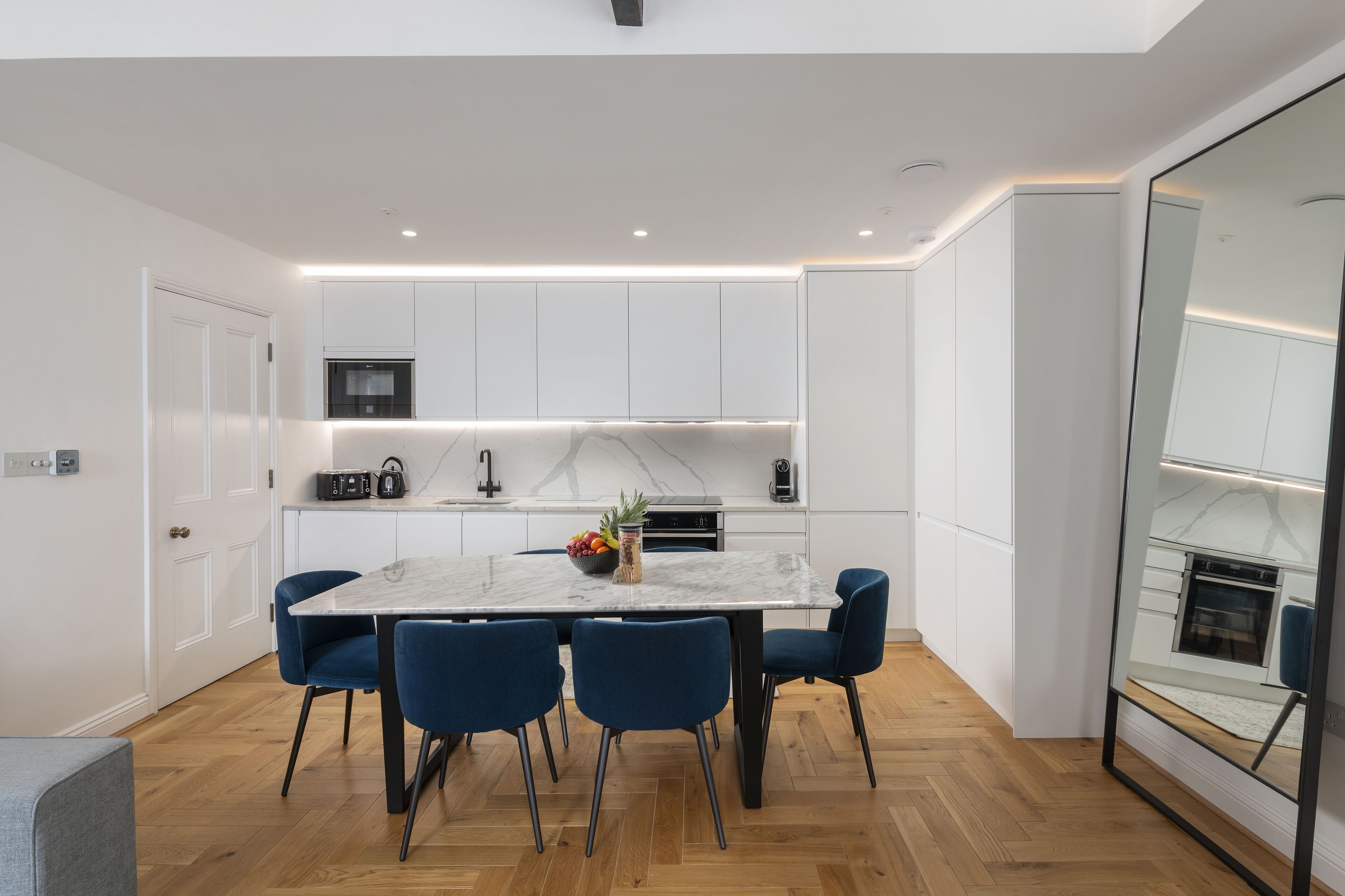 A modern kitchen with white cabinetry, a marble countertop, and a central island with chairs.
