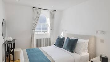 A modern hotel room with a large bed, a bedside table, a small round table, and a window with curtains.