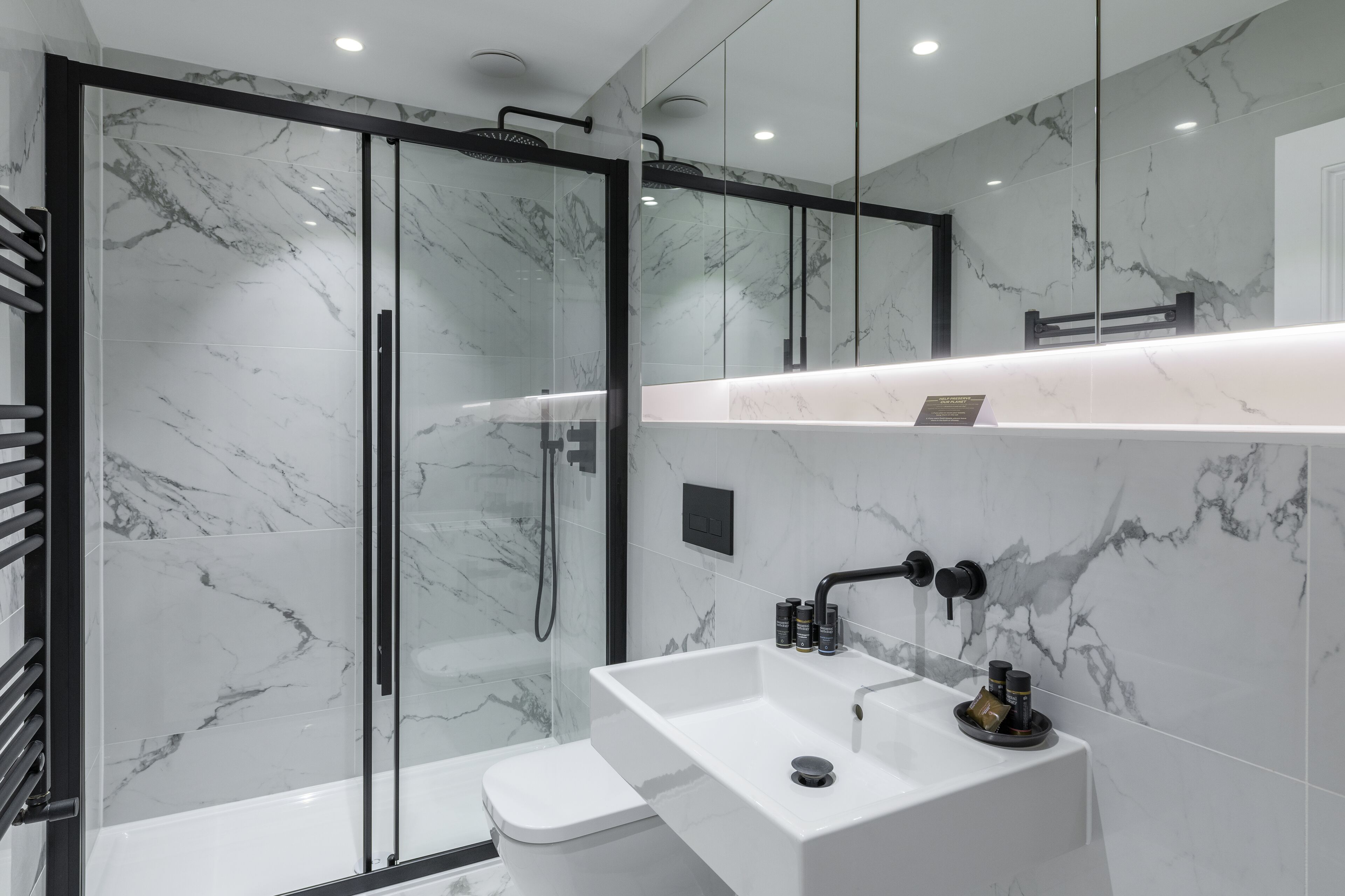 Une salle de bain moderne avec une douche à parois de verre, un lavabo blanc doté d’un plan de toilette en marbre et un robinet noir.