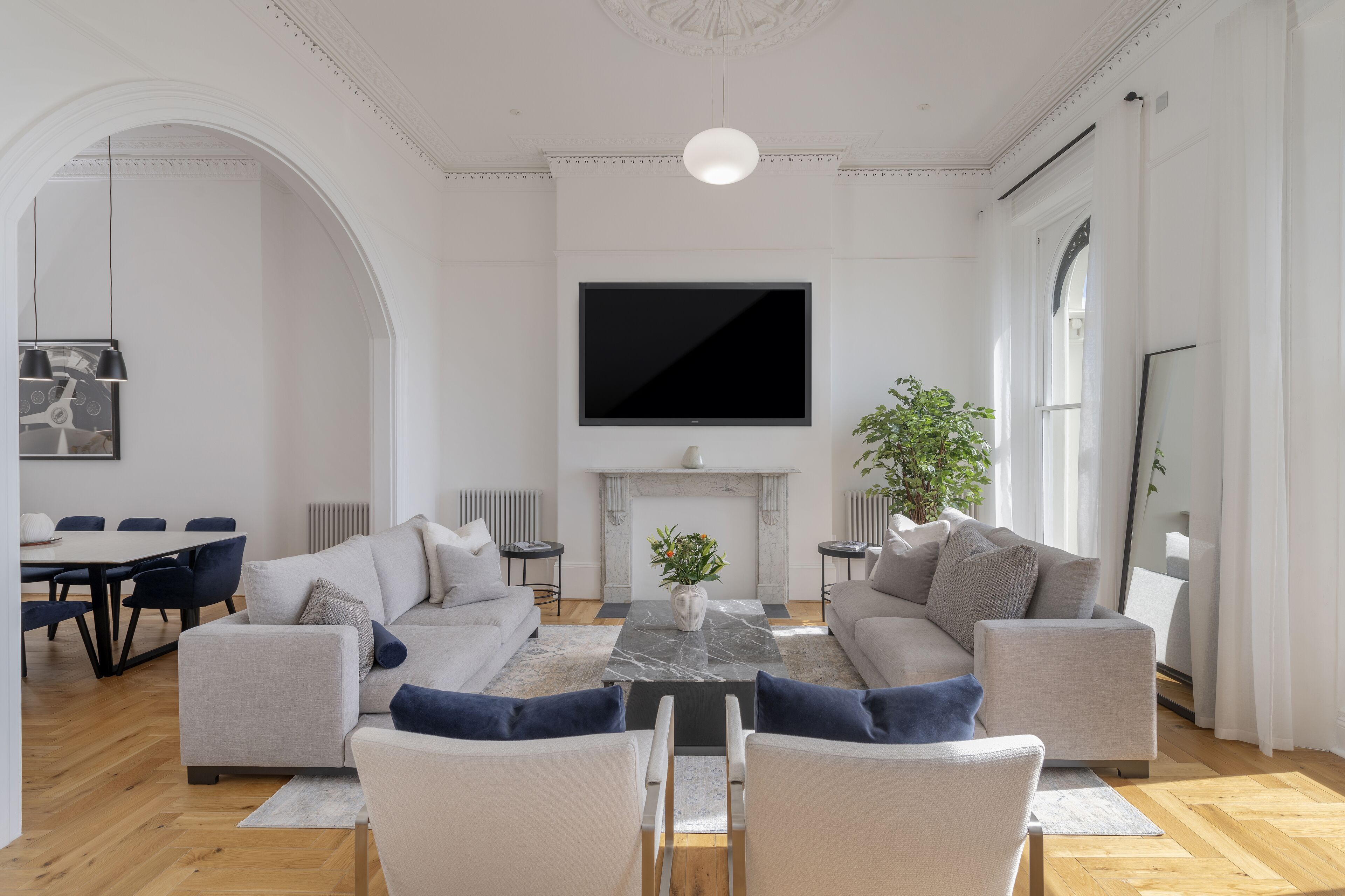 Een moderne woonkamer met een open haard, een grote flatscreen televisie en een eethoek met een tafel en stoelen.