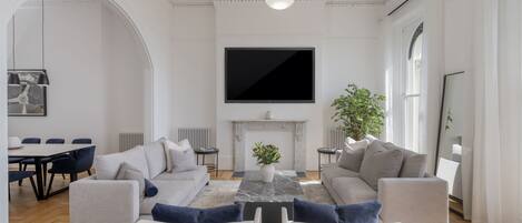 A modern living room with a fireplace, a large flat-screen TV, and a dining area with a table and chairs.
