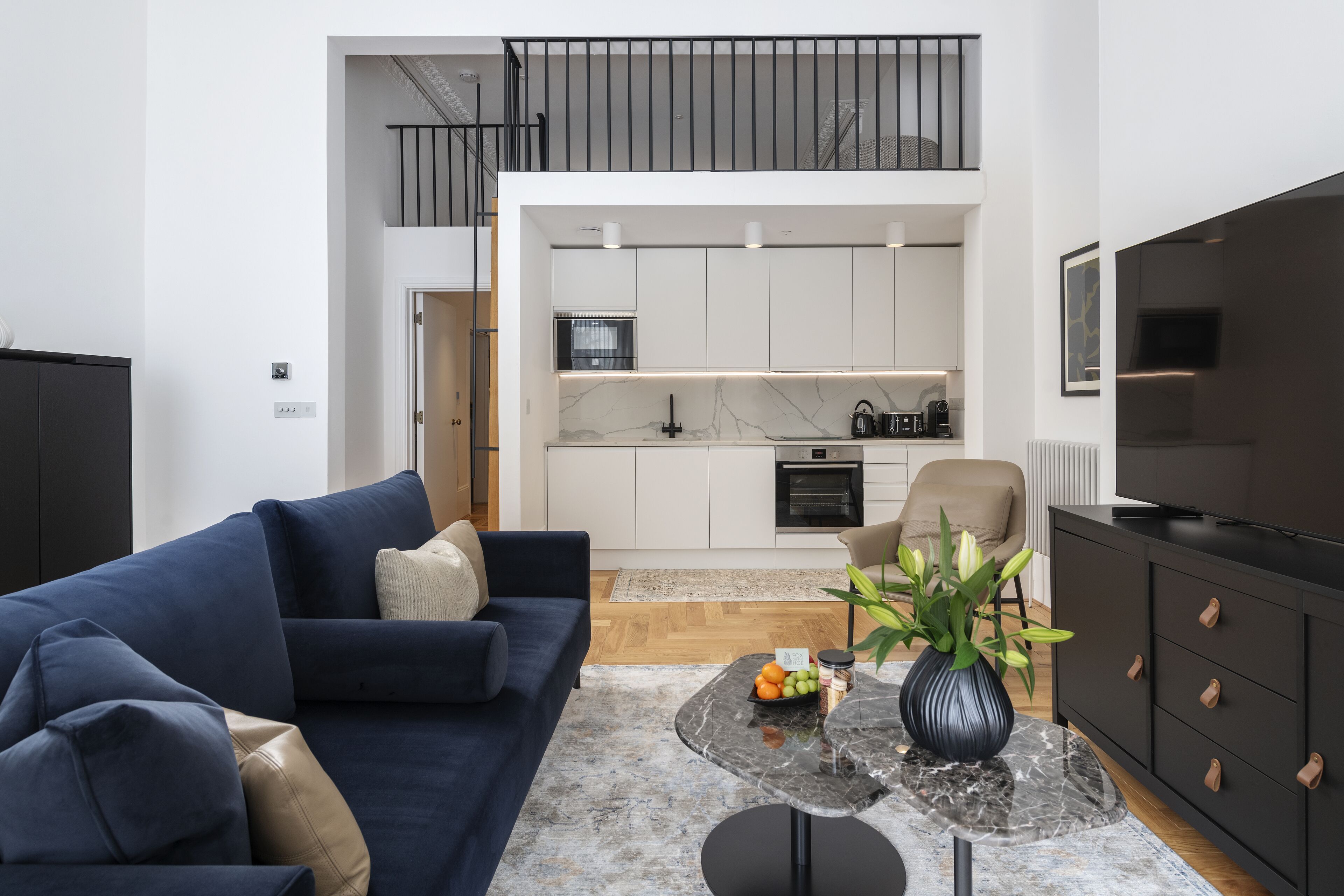 Een moderne woonkamer met een donkerblauwe bank, een marmeren salontafel en een zwarte tv-meubel.