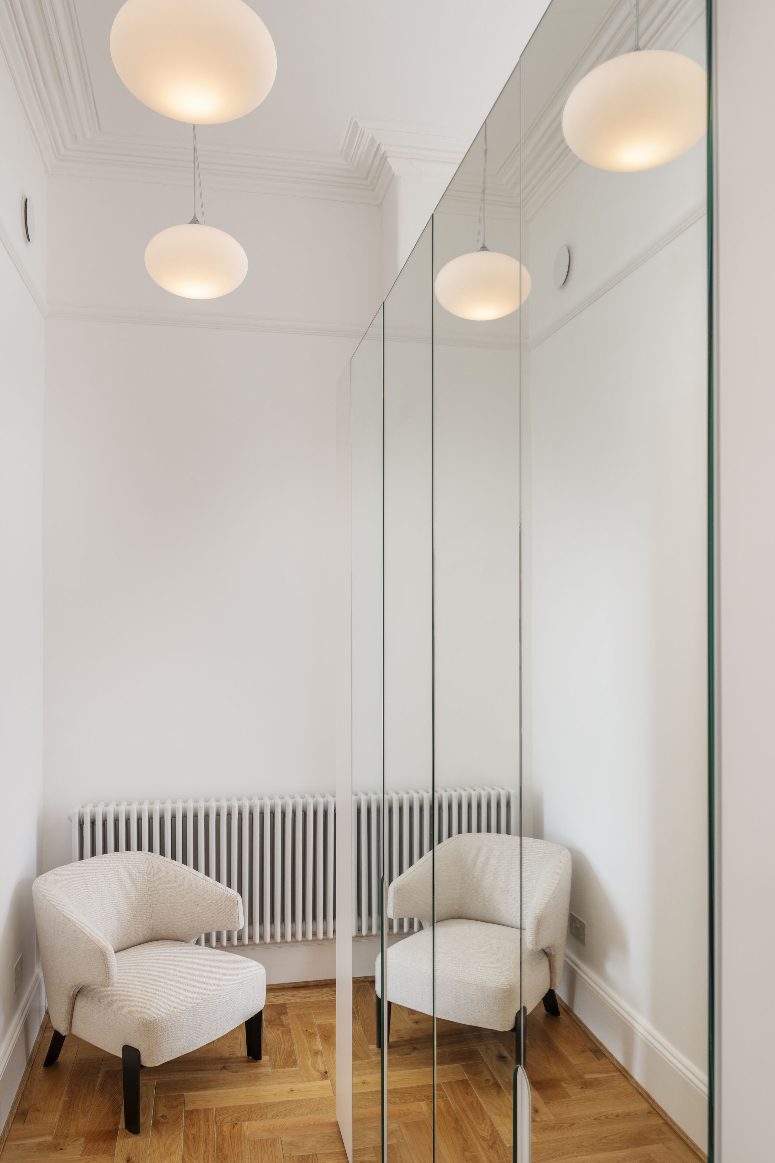 A modern room with a white armchair, a glass partition, and a radiator.