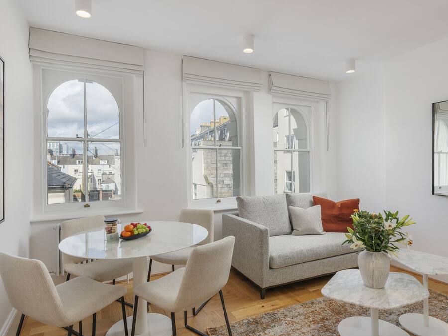Un salon moderne avec un canapé gris, une table ronde blanche et des chaises. On peut voir une plante en pot sur une petite table blanche.