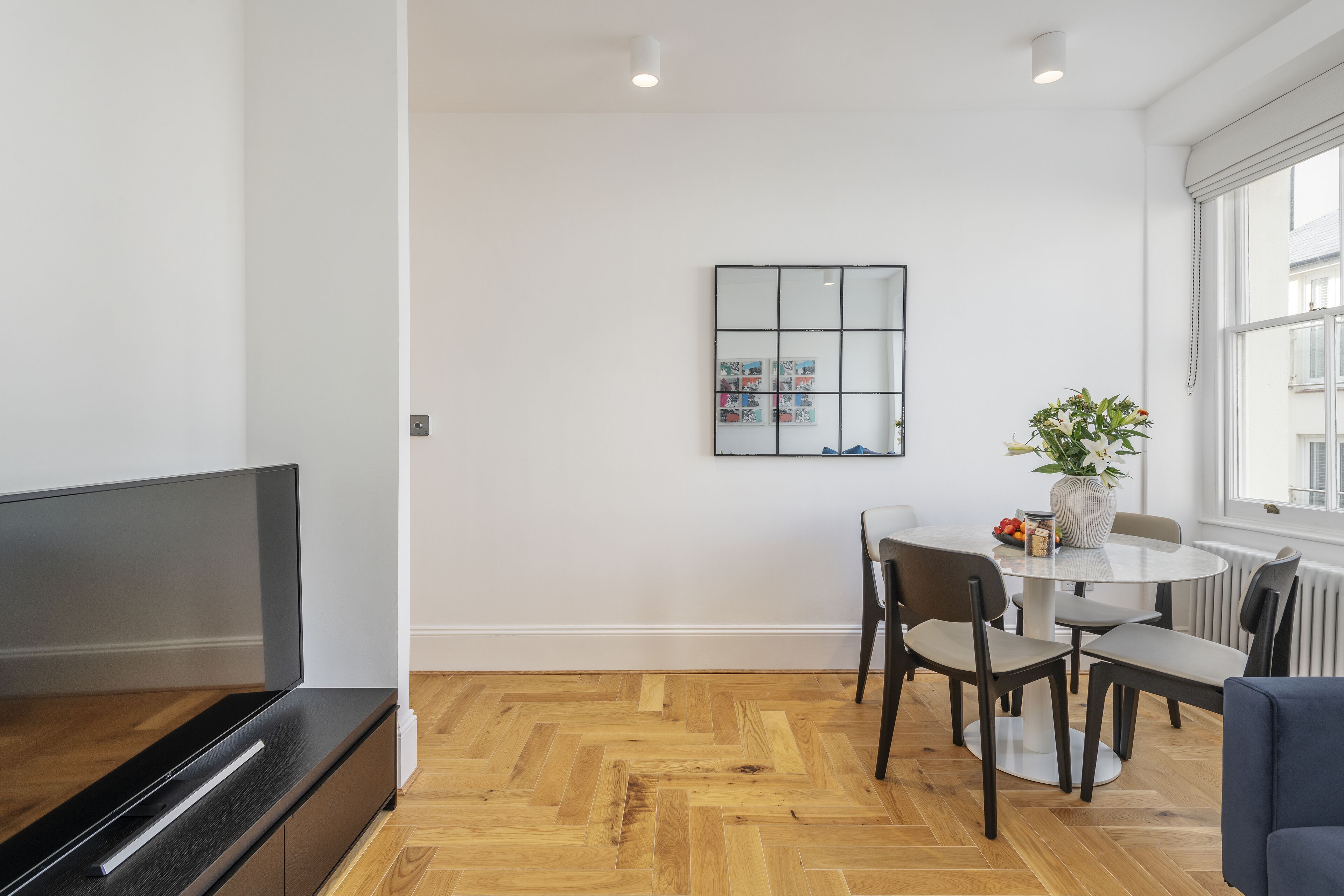 En moderne stue med et fladskærms-tv, et spisebord med stole, en potteplante og et billede i ramme på væggen.