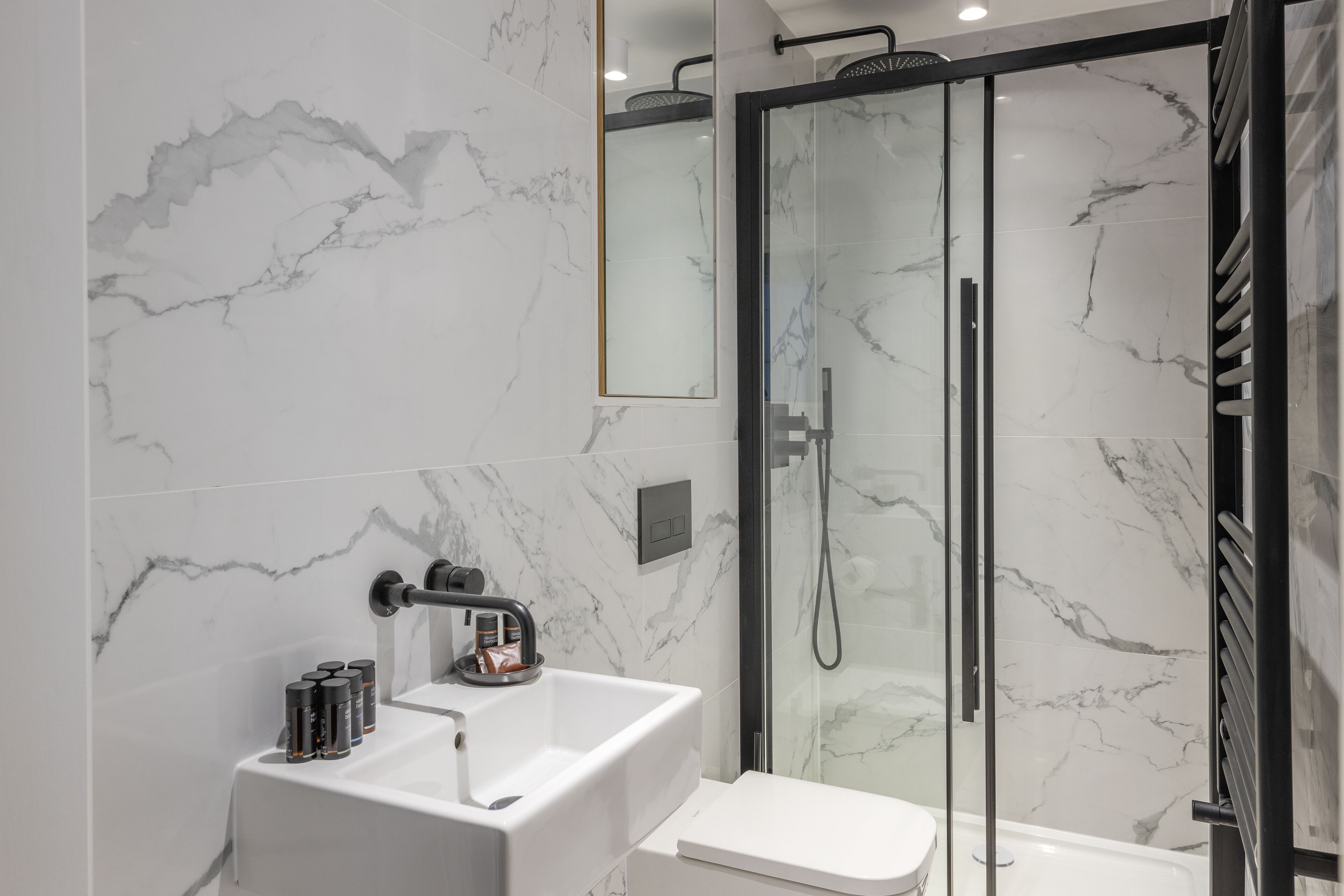 Et moderne badeværelse med en glasafskærmet brusekabine, en hvid vask og et toilet.