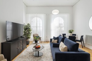Una sala moderna con un mueble de TV negro, un sofá azul, una mesa de comedor con sillas y una planta en maceta.