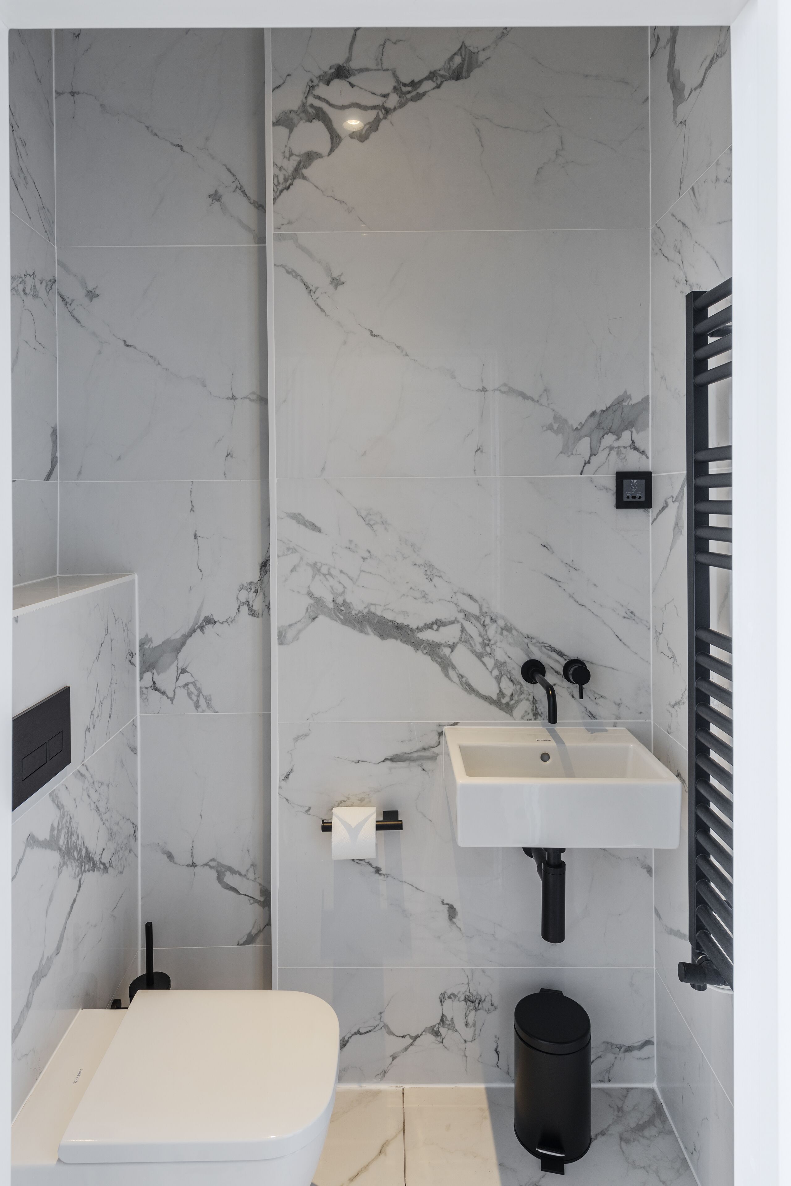 Un baño con inodoro, lavamanos y un cubo de basura negro.