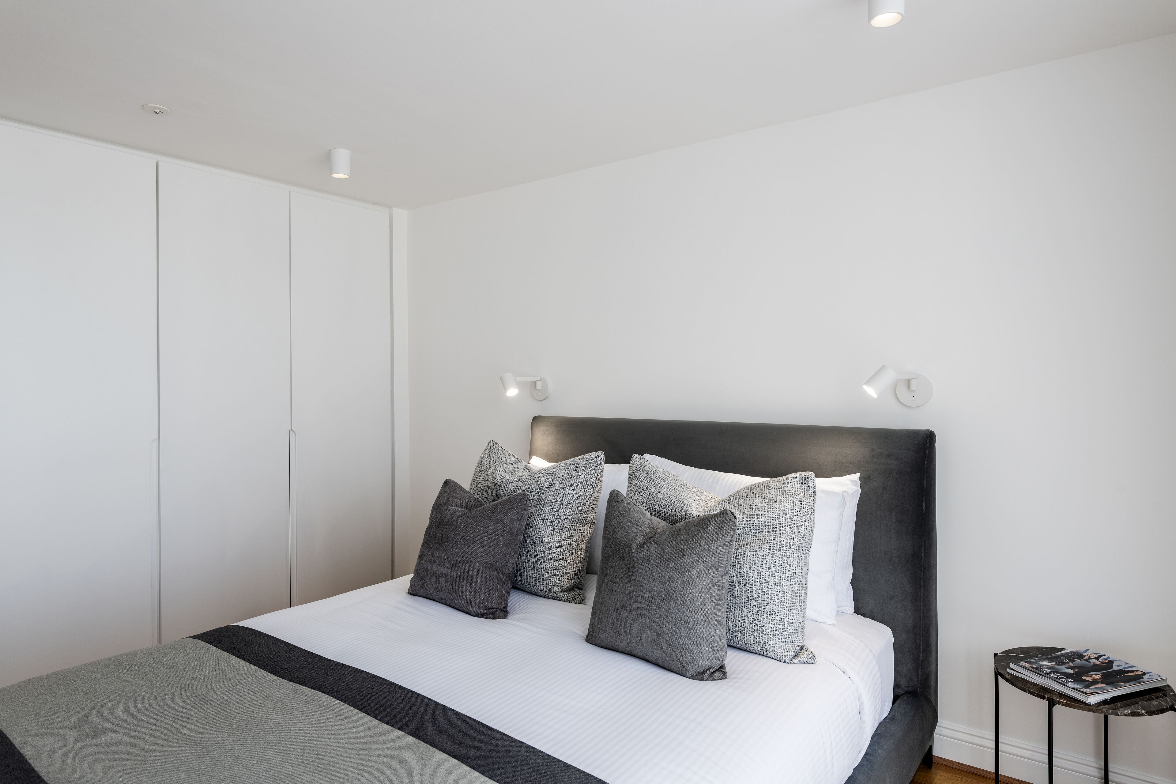 Un dormitorio moderno con una cama grande, ropa de cama gris y blanca, y un cabecero oscuro.