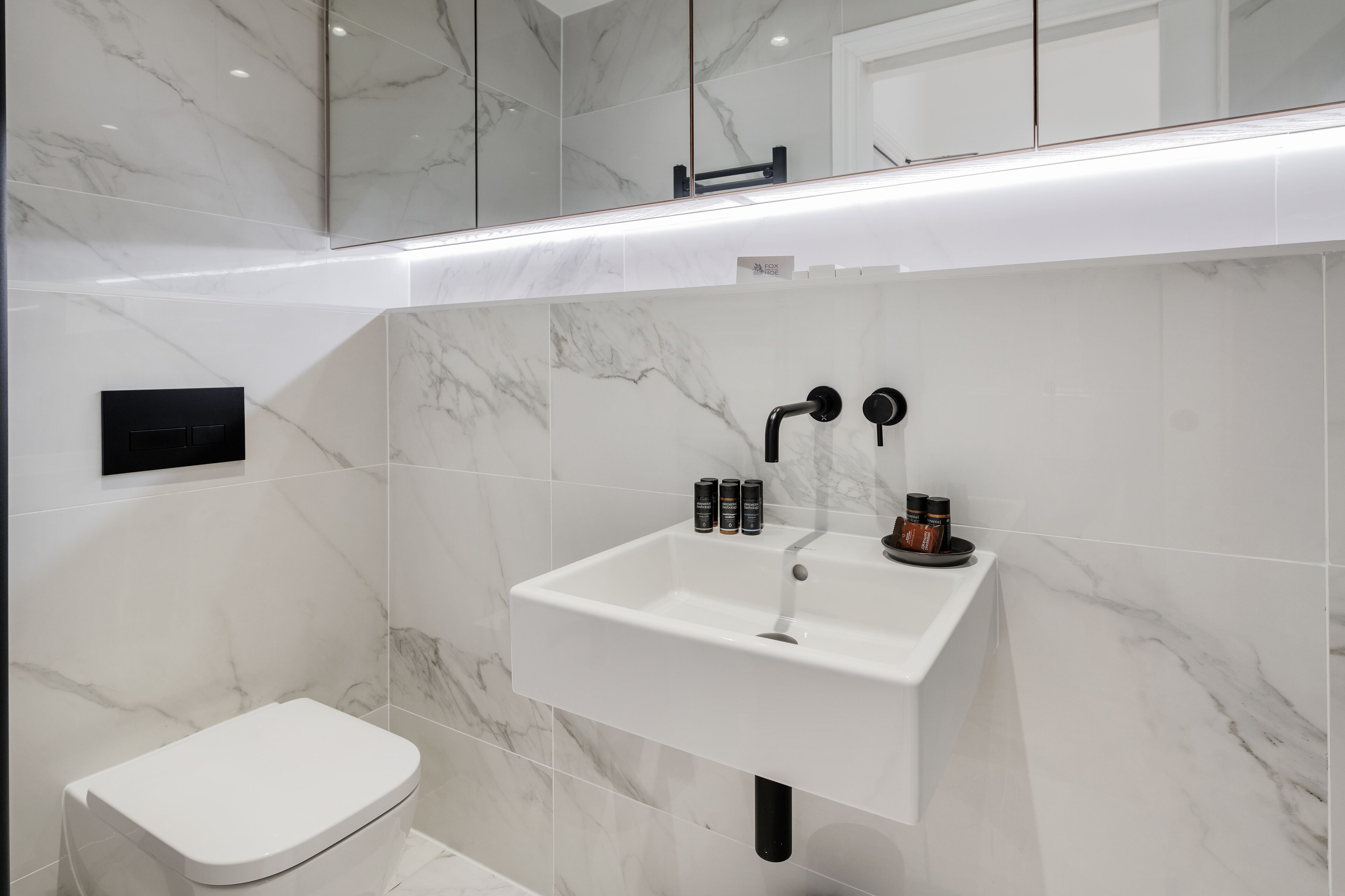 A modern bathroom with a white sink, black faucet, and marble tiles.