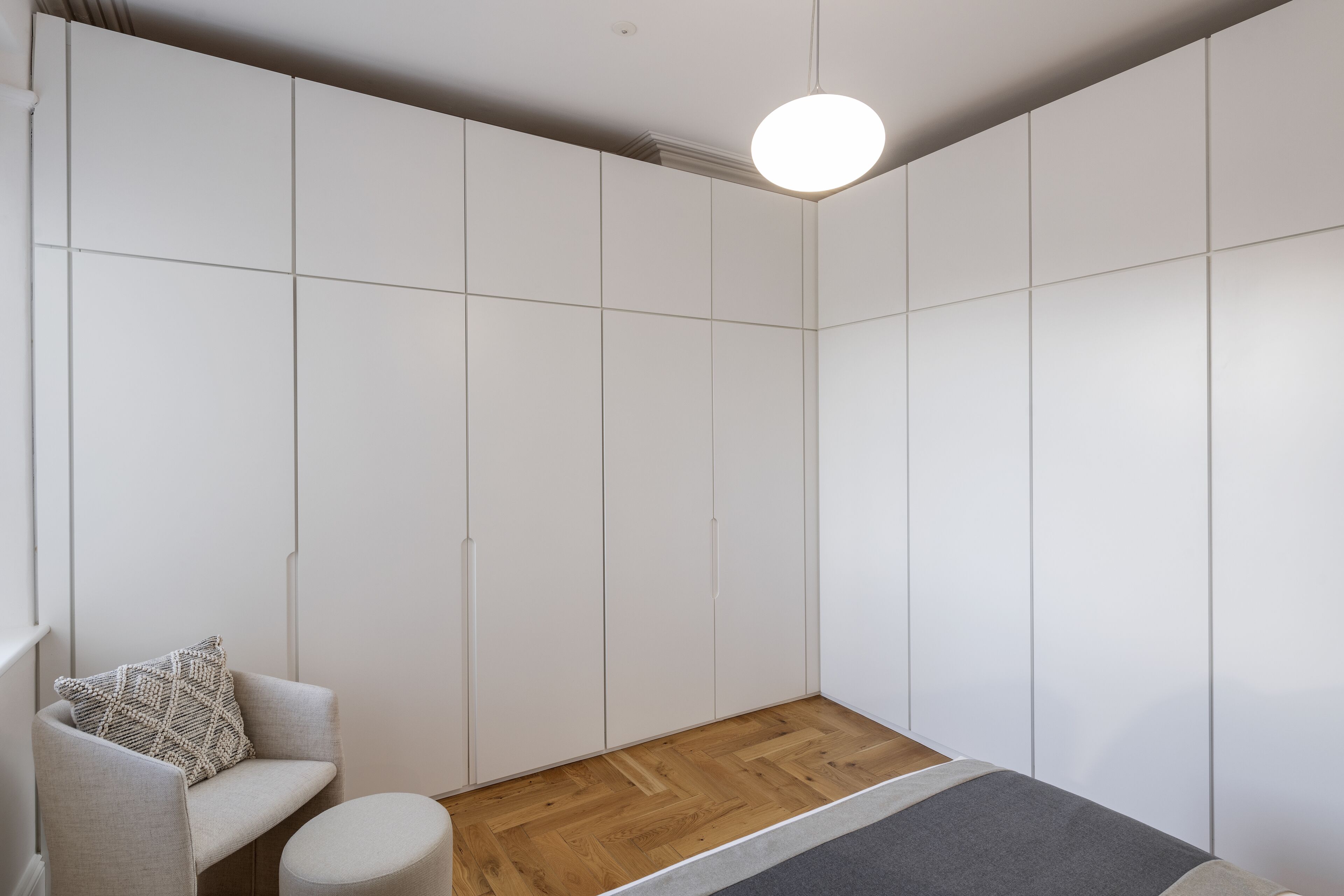 A modern room with a built-in wardrobe, a round light fixture, a wooden floor, and a grey sofa with a patterned pillow.