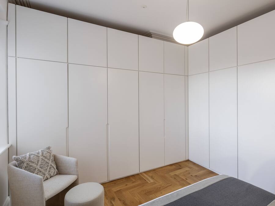 A modern room with a built-in wardrobe, a round light fixture, a wooden floor, and a grey sofa with a patterned pillow.