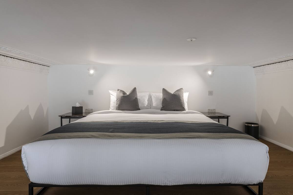 Quarto moderno com uma cama grande, duas mesas de cabeceira e um criado-mudo pequeno.