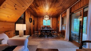 Una habitación acogedora con paredes y techo de madera, una mesa de comedor con sillas, un sofá y un ventanal con cortinas.