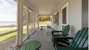 Een overdekt terras met uitzicht op het strand, groene Adirondack-stoelen en een klein tafeltje.