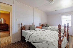 A bedroom with two beds, a dresser, and a window.