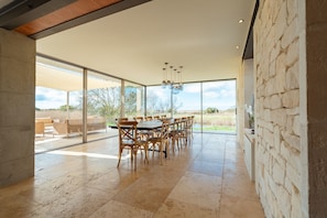 Un vaste espace dédié à la salle à manger, avec une grande table et des chaises, de grandes fenêtres et une vue sur l’extérieur.